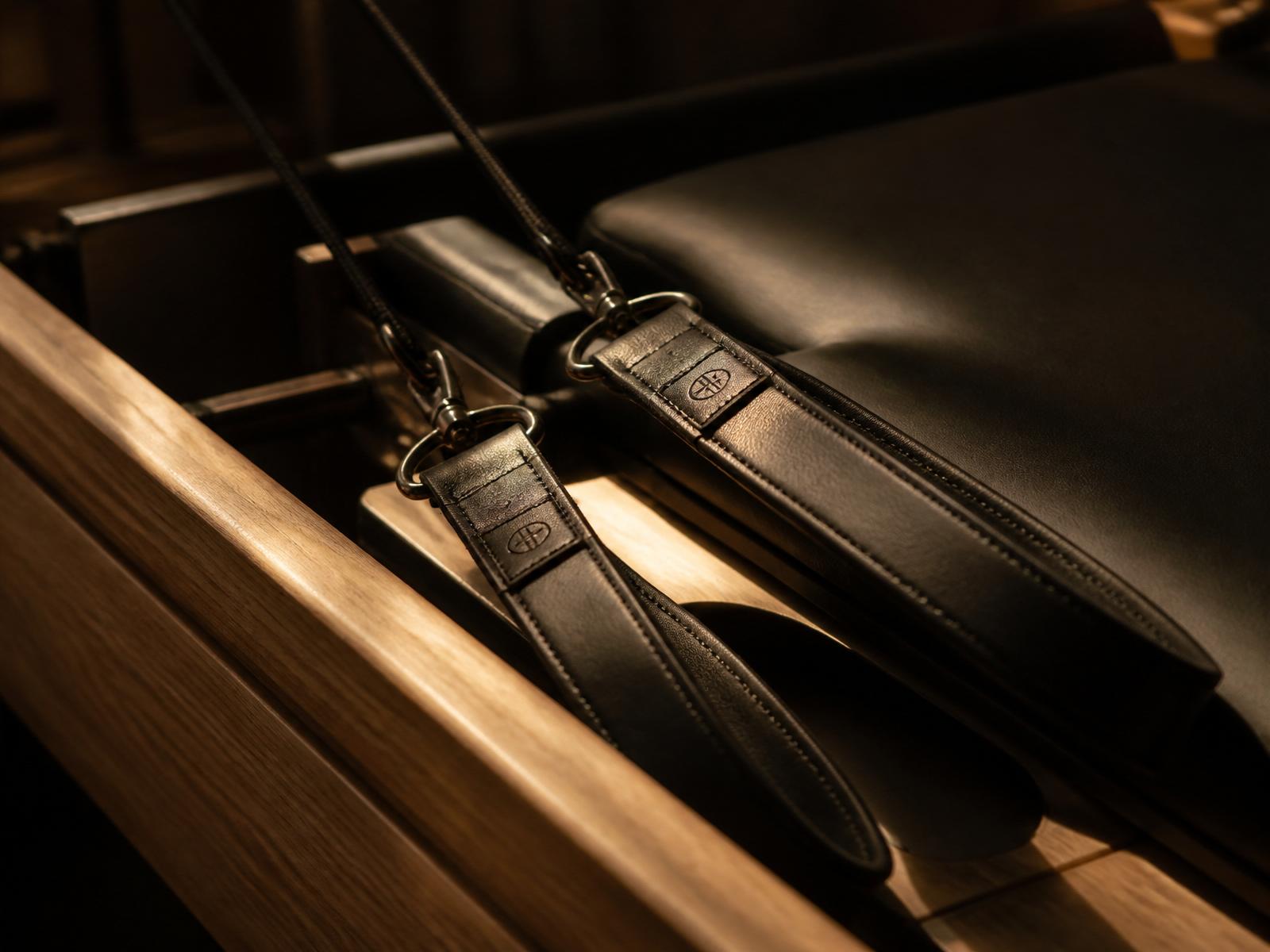 Detail of leather reformer straps against warm wood, low light